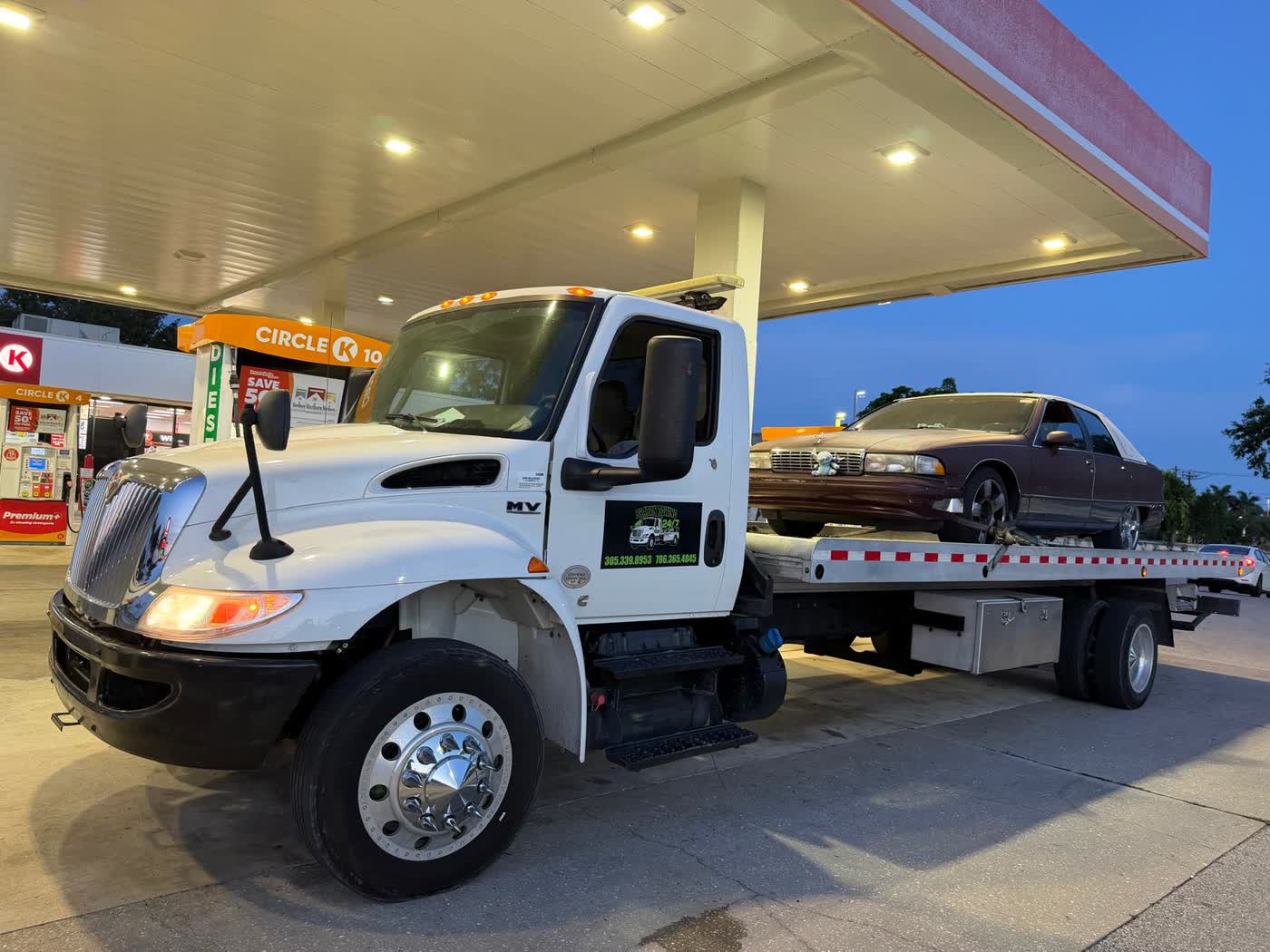 Camión de Brayan Towing cargando un auto al anochecer en una gasolinera